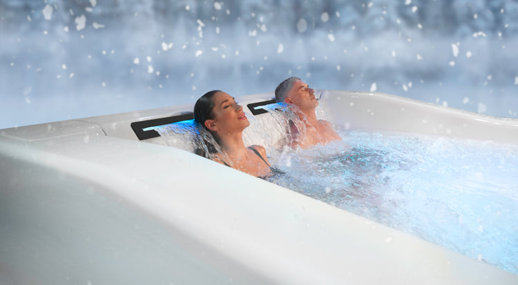 Two people relaxing in a hot tub with a snowy landscape in the background, factory direct hot tub