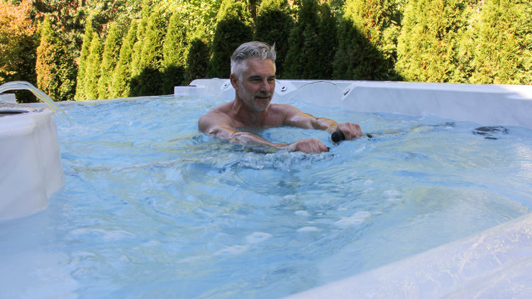 Man relaxing in a hot tub with greenery in the background, factory direct hot tub